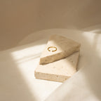 The Open Diamond Duo Ring, a minimalistic jewelry piece, is displayed on two beige stone slabs, highlighted by gentle sunlight and delicate shadows.