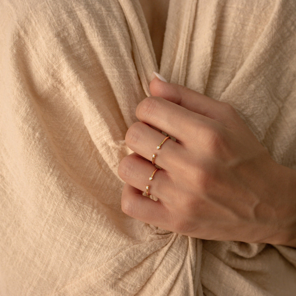 A hand wearing two gold rings, one of which is the Open Diamond Duo Ring, gently holds beige textured fabric near the chest.