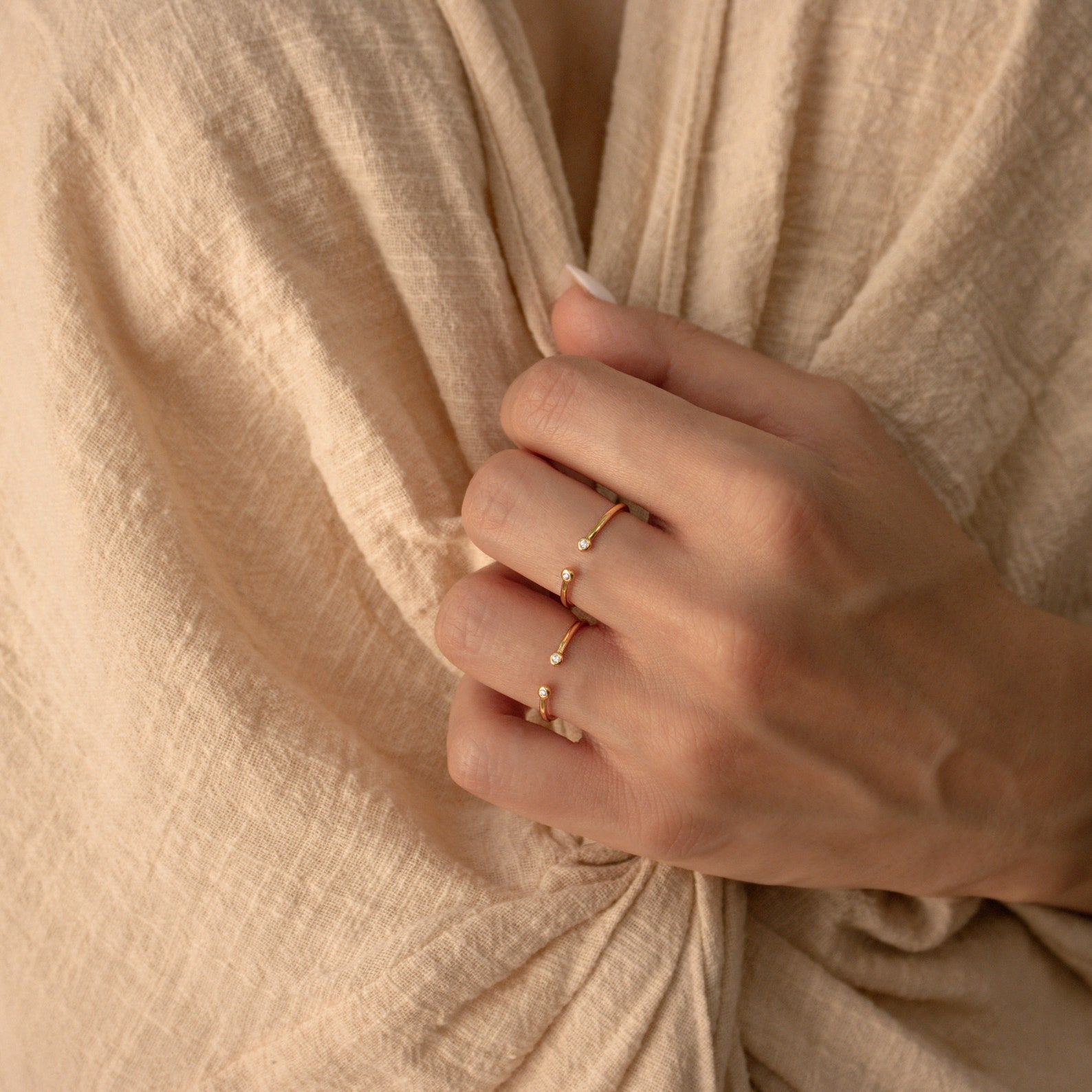 A hand wearing two gold rings, one of which is the Open Diamond Duo Ring, gently holds beige textured fabric near the chest.