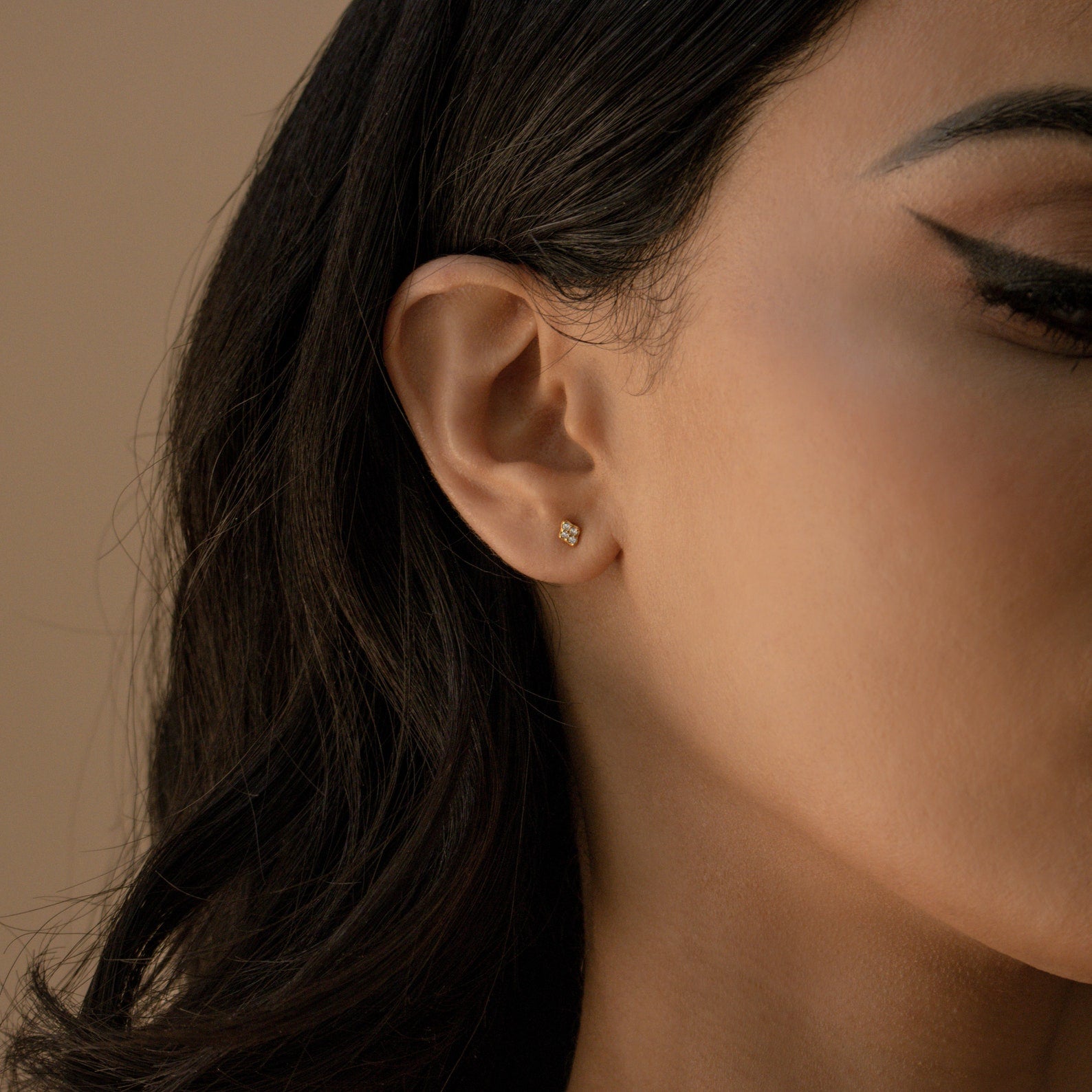 Close-up of a woman's ear wearing Avery Geometric Diamond Studs, paired with winged eyeliner makeup.