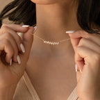 A woman holds the Bethany Baguette Bar Necklace, a delicate gold cable chain featuring a bar pendant, highlighting her manicured nails.