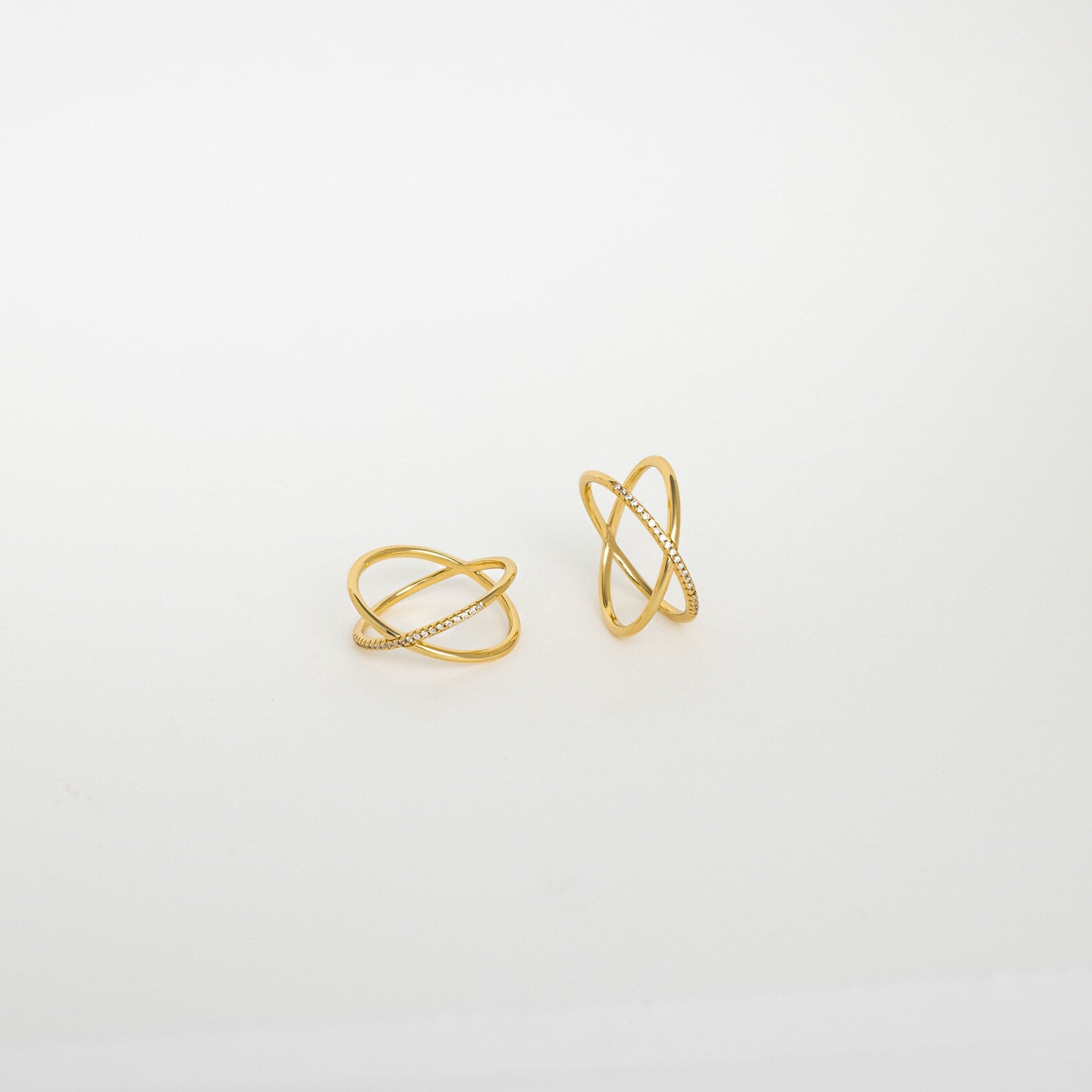 The Pave X Ring showcases two gold crossover bands, one adorned with pavé-set tiny diamonds, set against a plain white background.