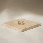 The Pave X Ring features a gold intersecting design with pavé diamonds, displayed on a square stone slab set against a neutral background.
