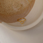 The Love Heart Knot Ring, featuring a heart-shaped knot design, is displayed gracefully in a speckled ceramic bowl.