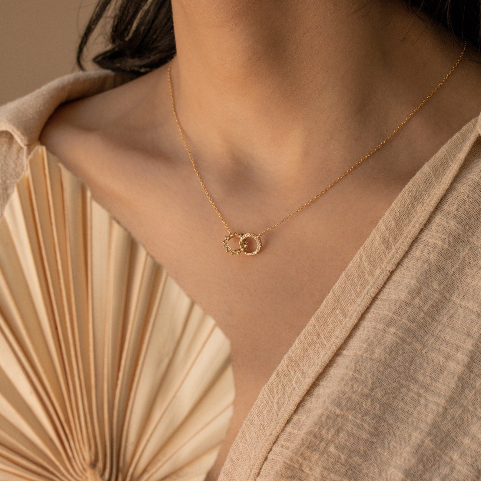 A woman wearing the Sun & Moon Eternity Necklace, featuring two interlocking circles, paired with a cream textured top.