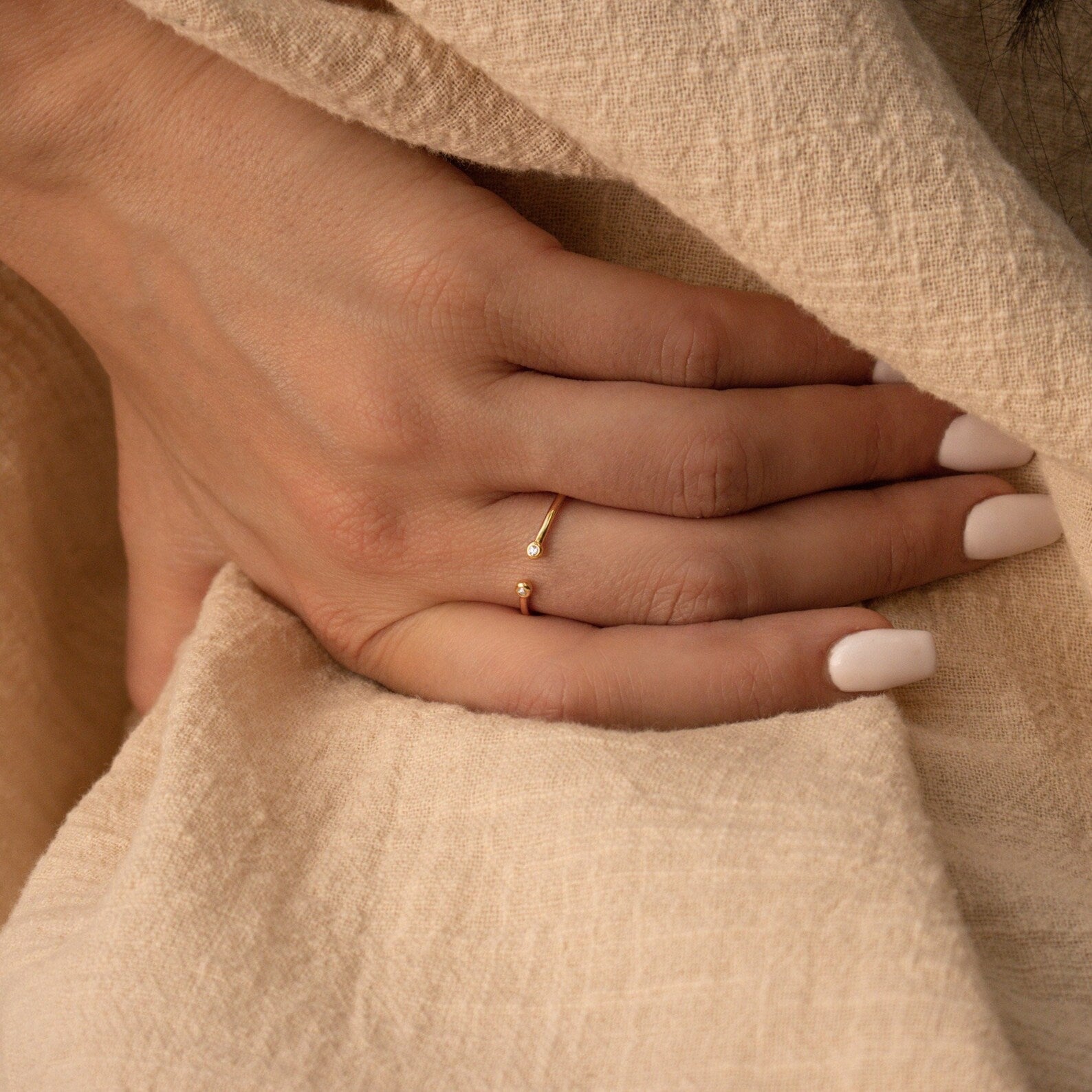 A hand with light pink nails wears the Open Diamond Duo Ring—a delicate, adjustable piece—resting on beige textured fabric.