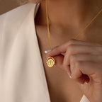 A person in a white top holds the Zodiac Spinner Necklace, showcasing its round pendant with an intricate astrological design.