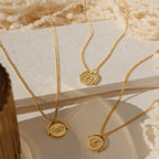 Three Zodiac Spinner Necklaces with round engraved astrological pendants are displayed on textured cream surfaces in sunlight.