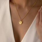 A woman wearing the Zodiac Spinner Necklace—a gold coin pendant with an elegant astrological design—pairs it with a white V-neck top.