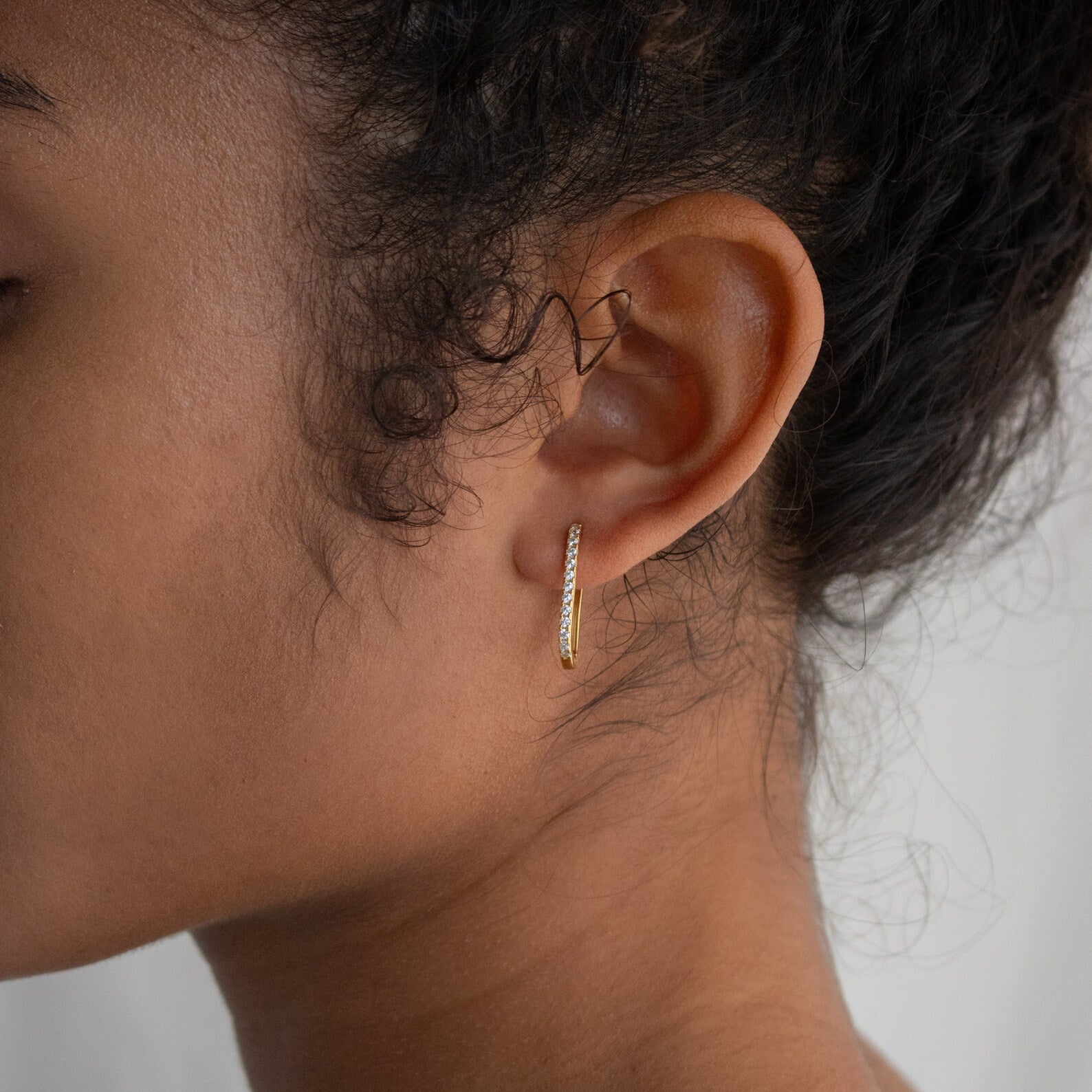 Close-up of a woman's ear adorned with Pave Link Earrings; her curly hair is pulled back, accentuating the delicate gold design.