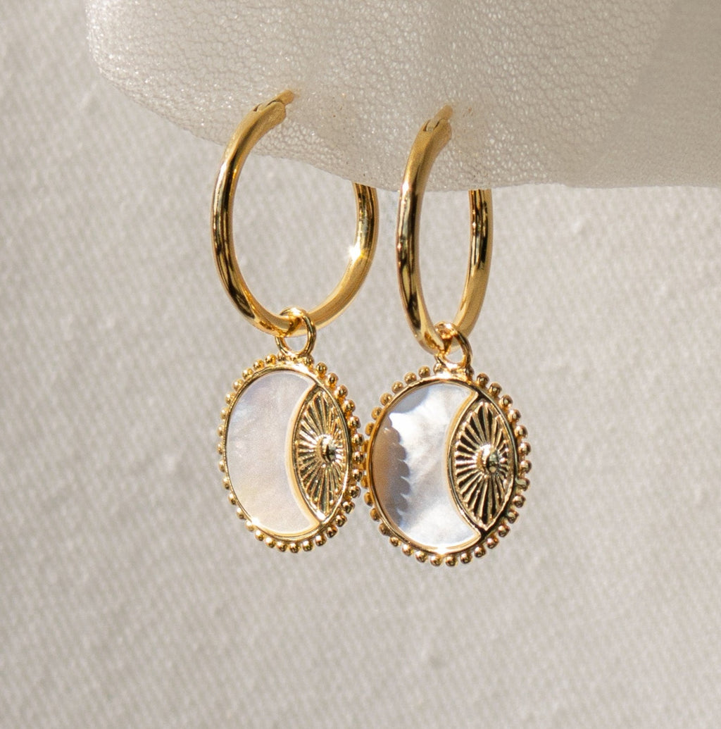 Pia Pearl Coin Hoops feature gold hoops with round white mother-of-pearl pendants and decorative gold details, adding a touch of boho elegance to any outfit.