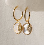 Pia Pearl Coin Hoops feature gold hoops with round white mother-of-pearl pendants and decorative gold details, adding a touch of boho elegance to any outfit.