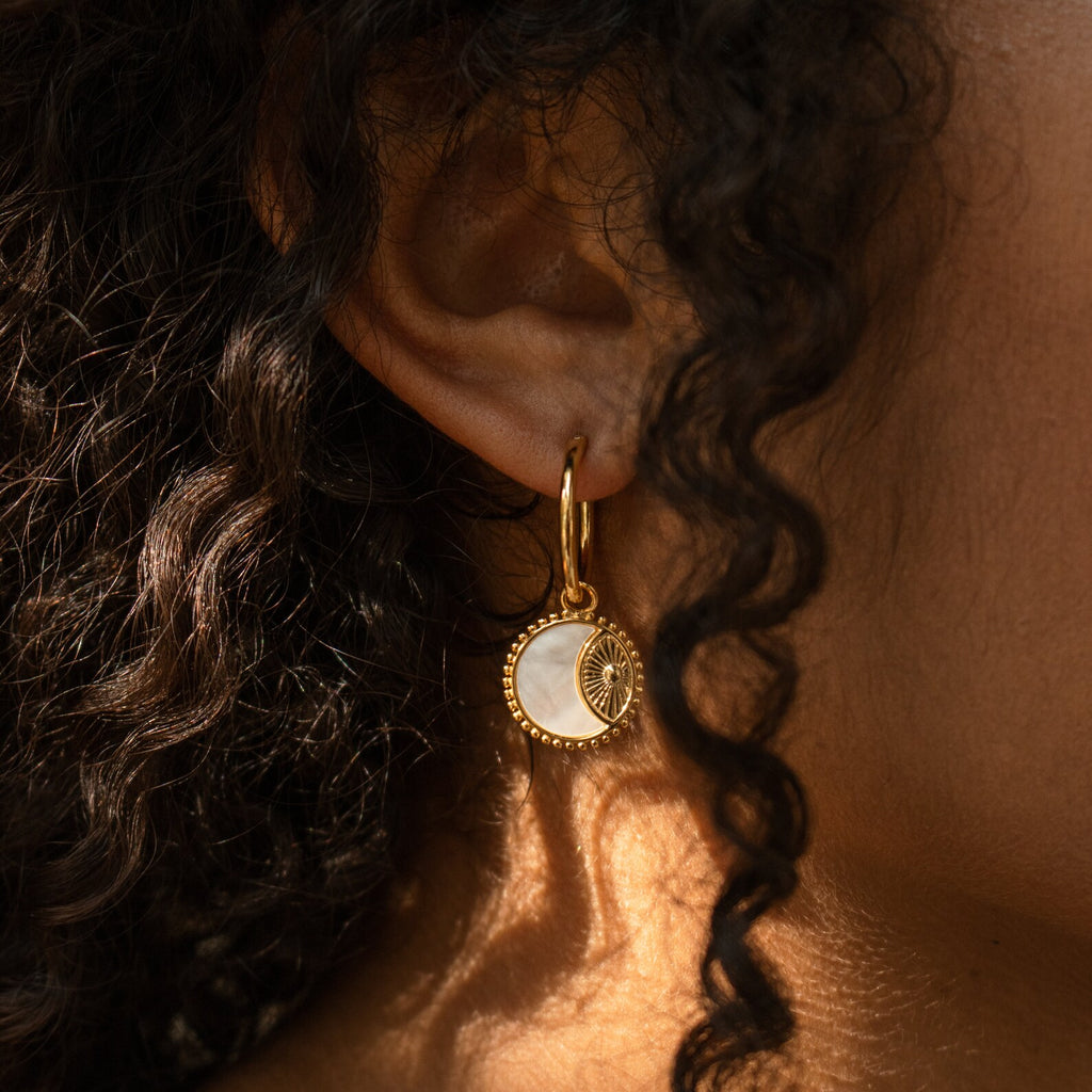 Close-up of an ear wearing Pia Pearl Coin Hoops—gold hoop earrings with a round, white and gold sunburst coin pendant—ideal for boho earring lovers.