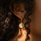 Close-up of an ear wearing Pia Pearl Coin Hoops—gold hoop earrings with a round, white and gold sunburst coin pendant—ideal for boho earring lovers.