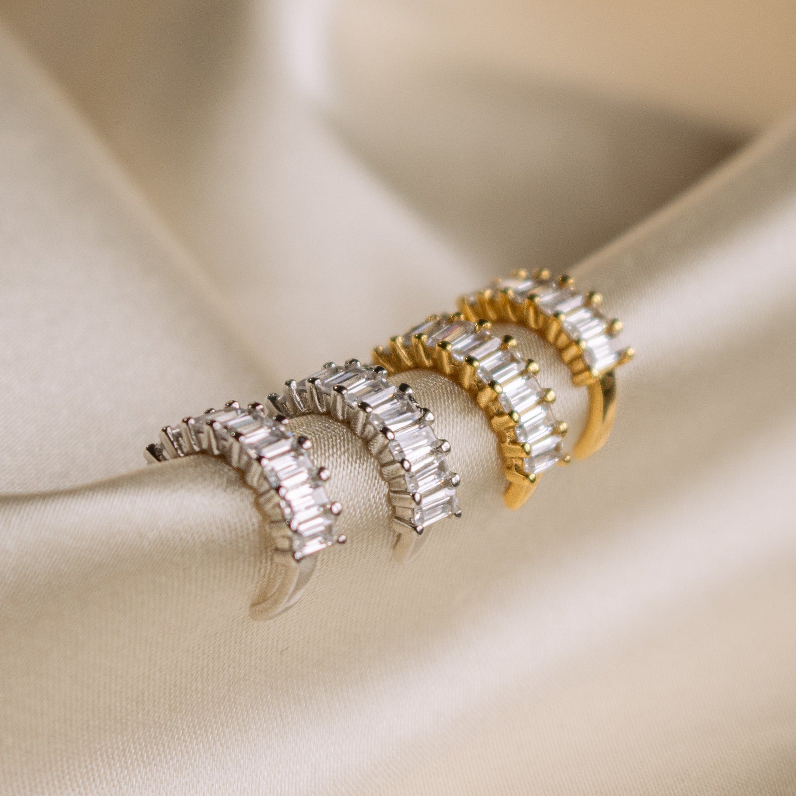 Three pairs of hoop earrings—two silver, one gold—displayed on beige satin add style to your look and perfectly complement the Baguette Ear Cuffs.