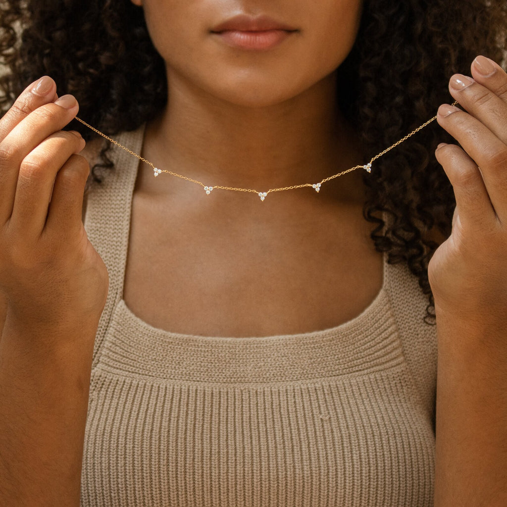 A woman holds the Hana Diamond Station Necklace with small diamond-shaped pendants near her neck, perfect for layering with other favorites.