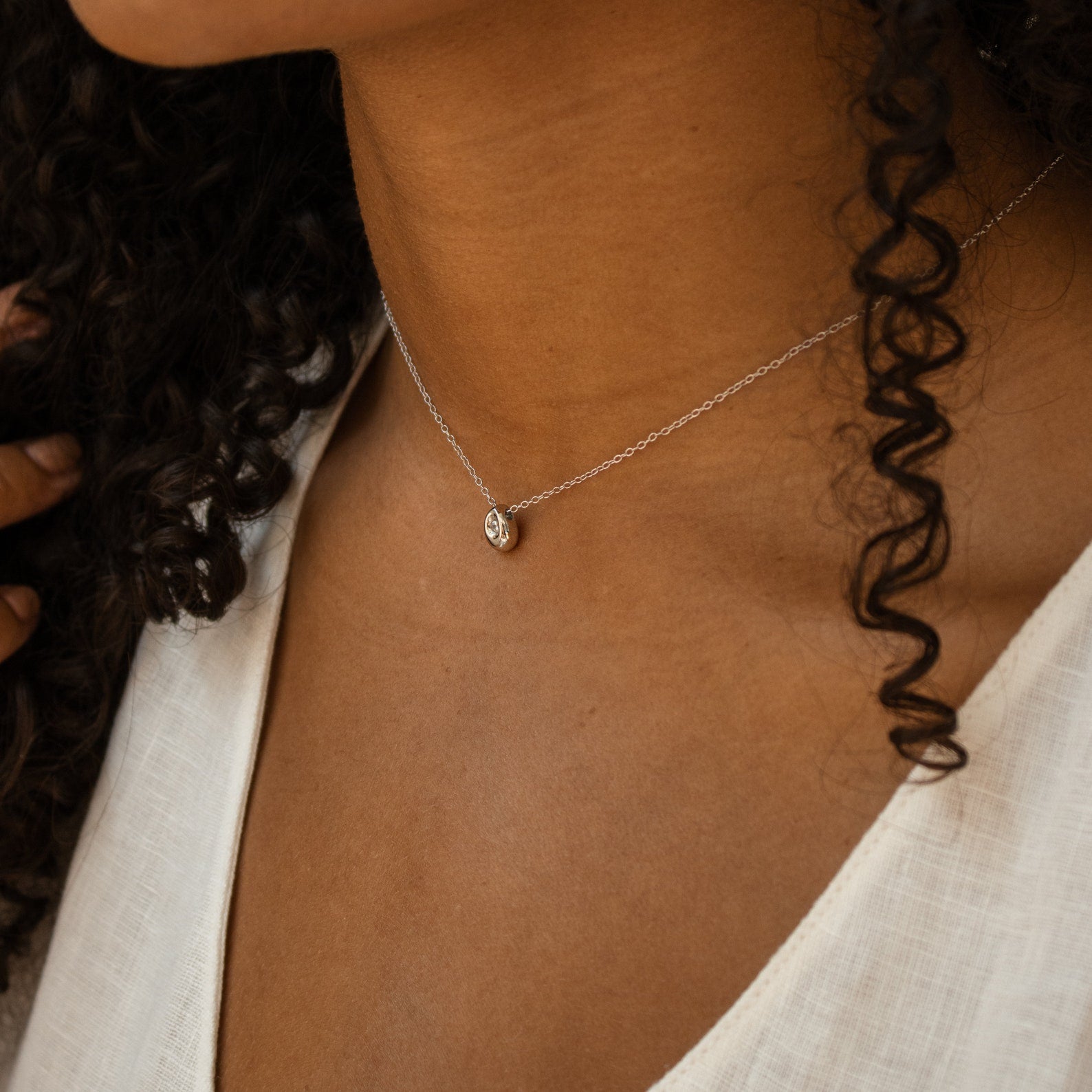A woman wearing the Nugget Necklace, a delicate and dainty piece with a small pendant, paired with a white top.