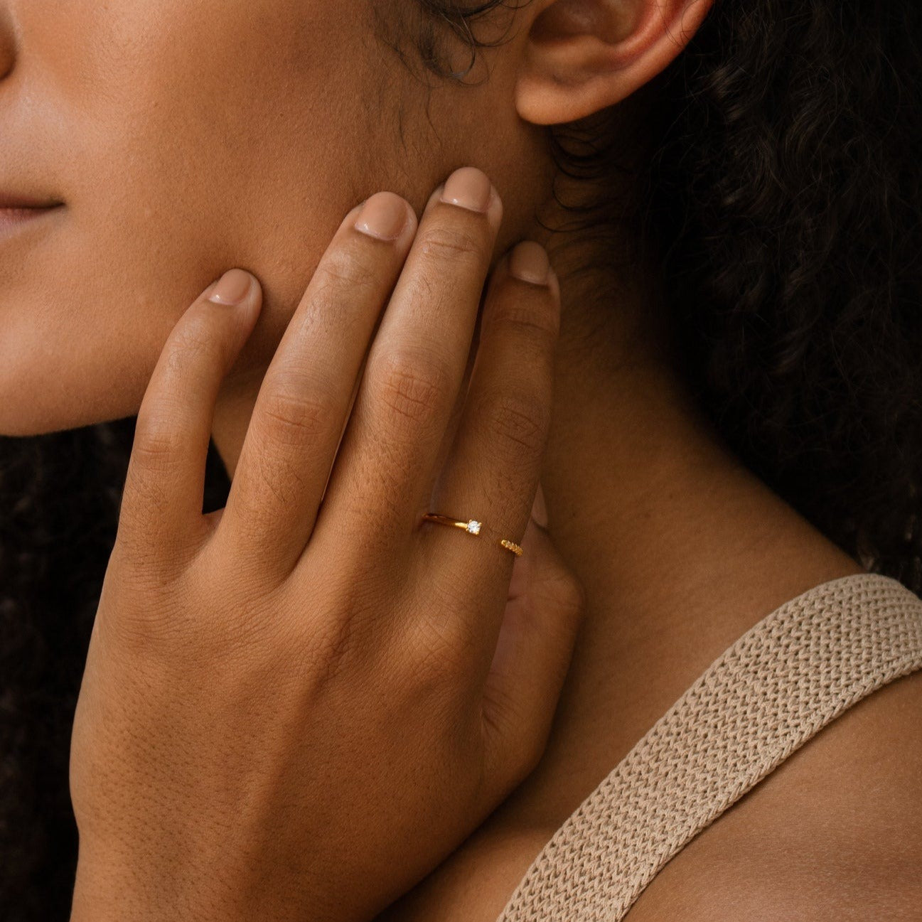 A woman wearing the Cecilia Pave Ring gently touches her face, dressed in a beige textured top.