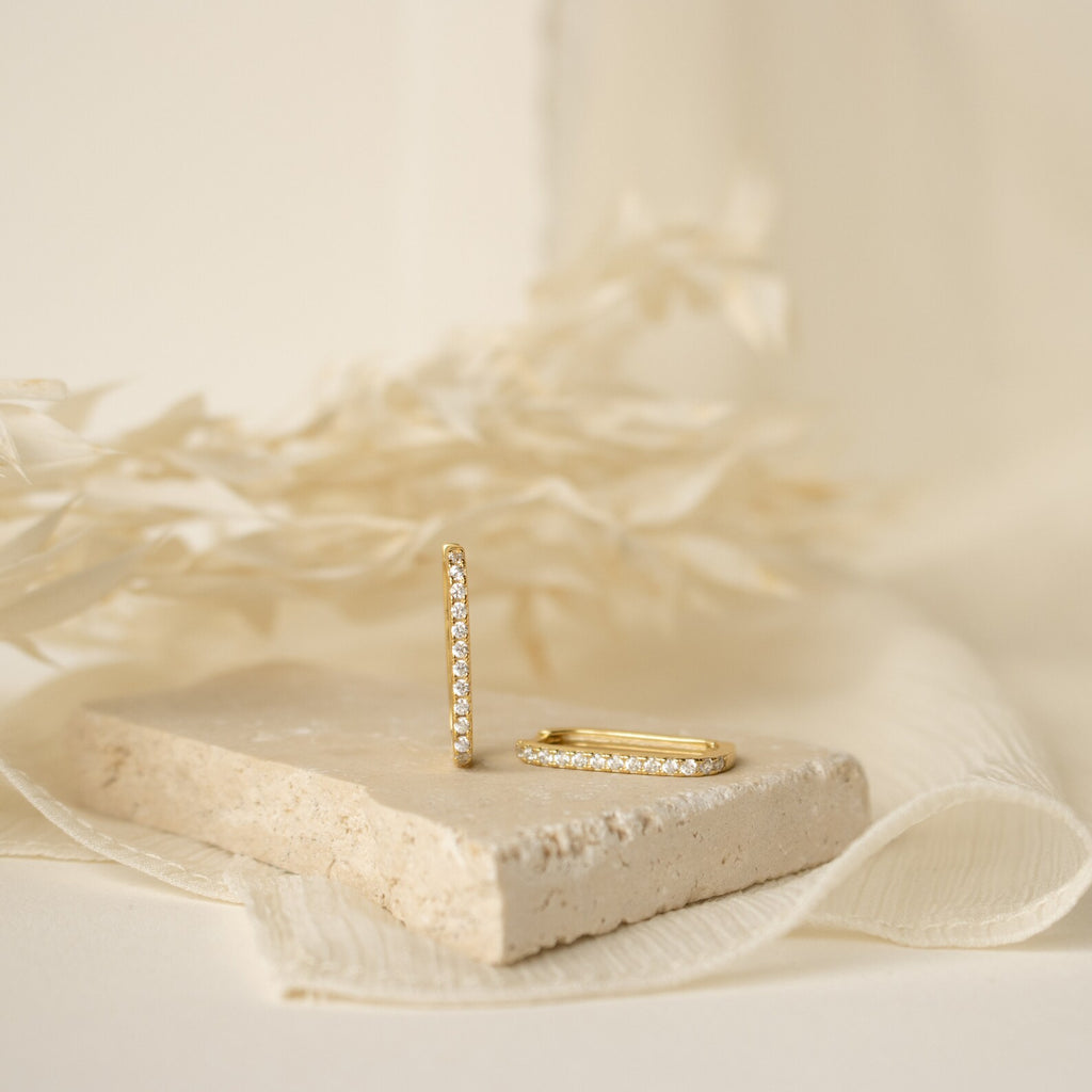 Pave Link Earrings featuring sparkling diamonds are displayed on a stone slab, with dried foliage accenting the background.
