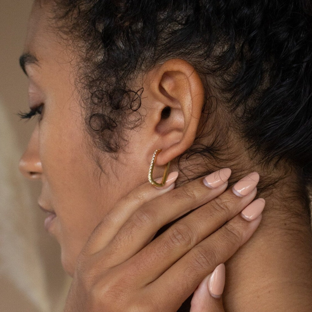 Woman with curly hair touching her neck, wearing Pave Link Earrings and nude nail polish for an effortlessly chic look.