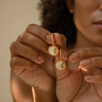 A woman holding the Pia Pearl Coin Hoops, featuring delicate mother of pearl accents.