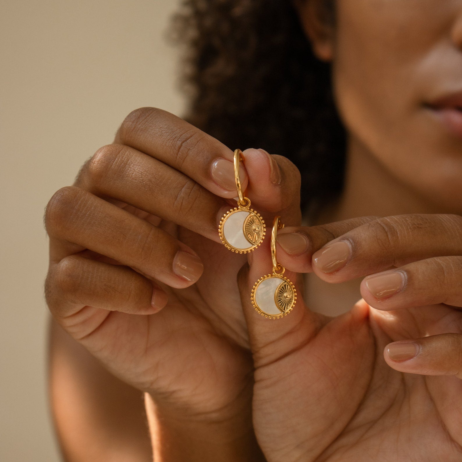 A woman holding the Pia Pearl Coin Hoops, featuring delicate mother of pearl accents.