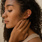 A woman with curly hair, eyes closed, gently touches her neck and ear while wearing Baguette Ear Cuffs in silver.
