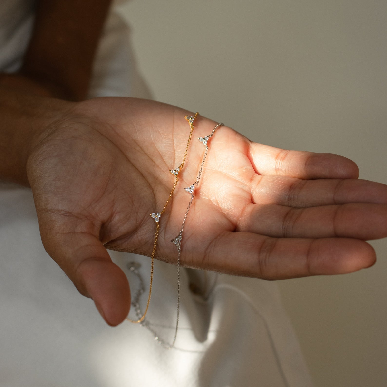 A hand holding delicate gold and silver chain bracelets with sparkling gems, perfect for pairing with the Hana Diamond Station Necklace.