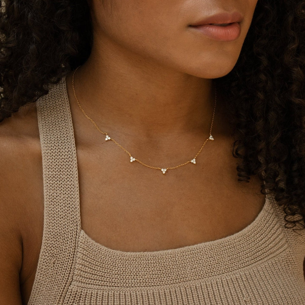 Close-up of a woman wearing a gold chain necklace adorned with evenly spaced clusters of three tiny clear stones, styled with a textured beige knit tank top.
