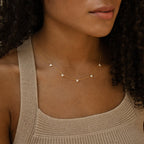 Close-up of a woman wearing a gold chain necklace adorned with evenly spaced clusters of three tiny clear stones, styled with a textured beige knit tank top.