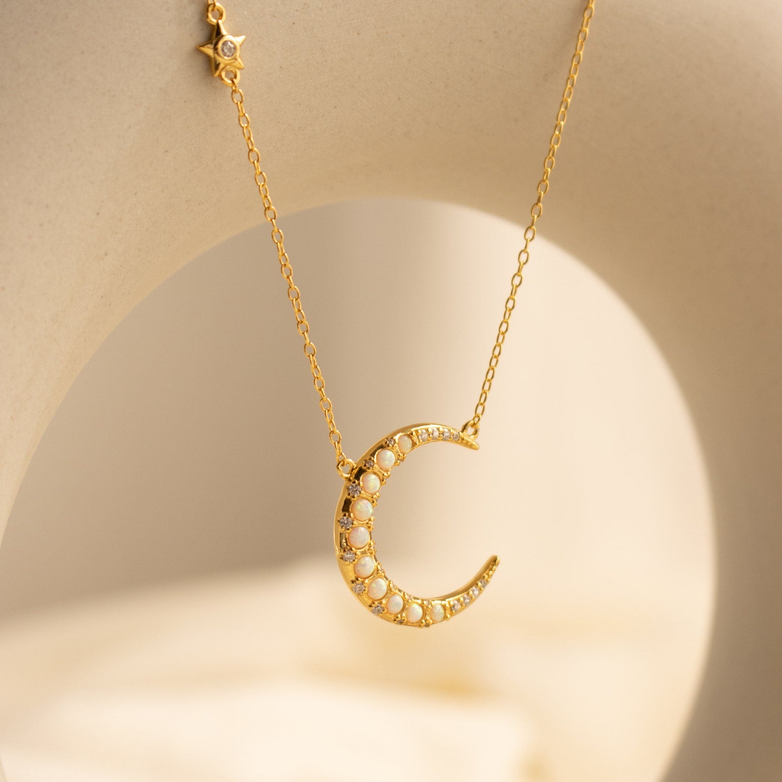 The Opal Crescent Moon Necklace features a gold crescent pendant with shimmering opals and a delicate star charm on the chain—a stylish boho accessory ideal for any occasion.