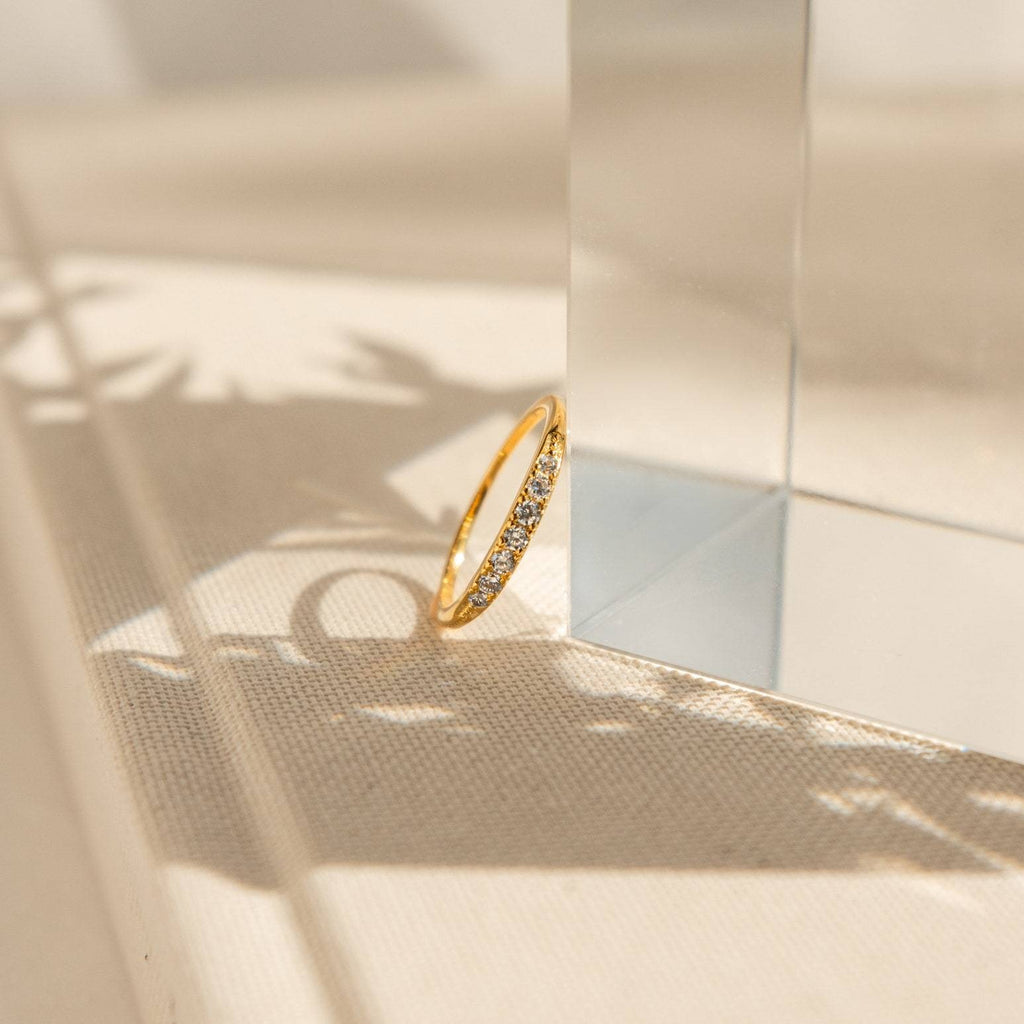 The Lace Pave Ring, a slim diamond band, is displayed on a clear glass block, its delicate shadow adding to its elegance.