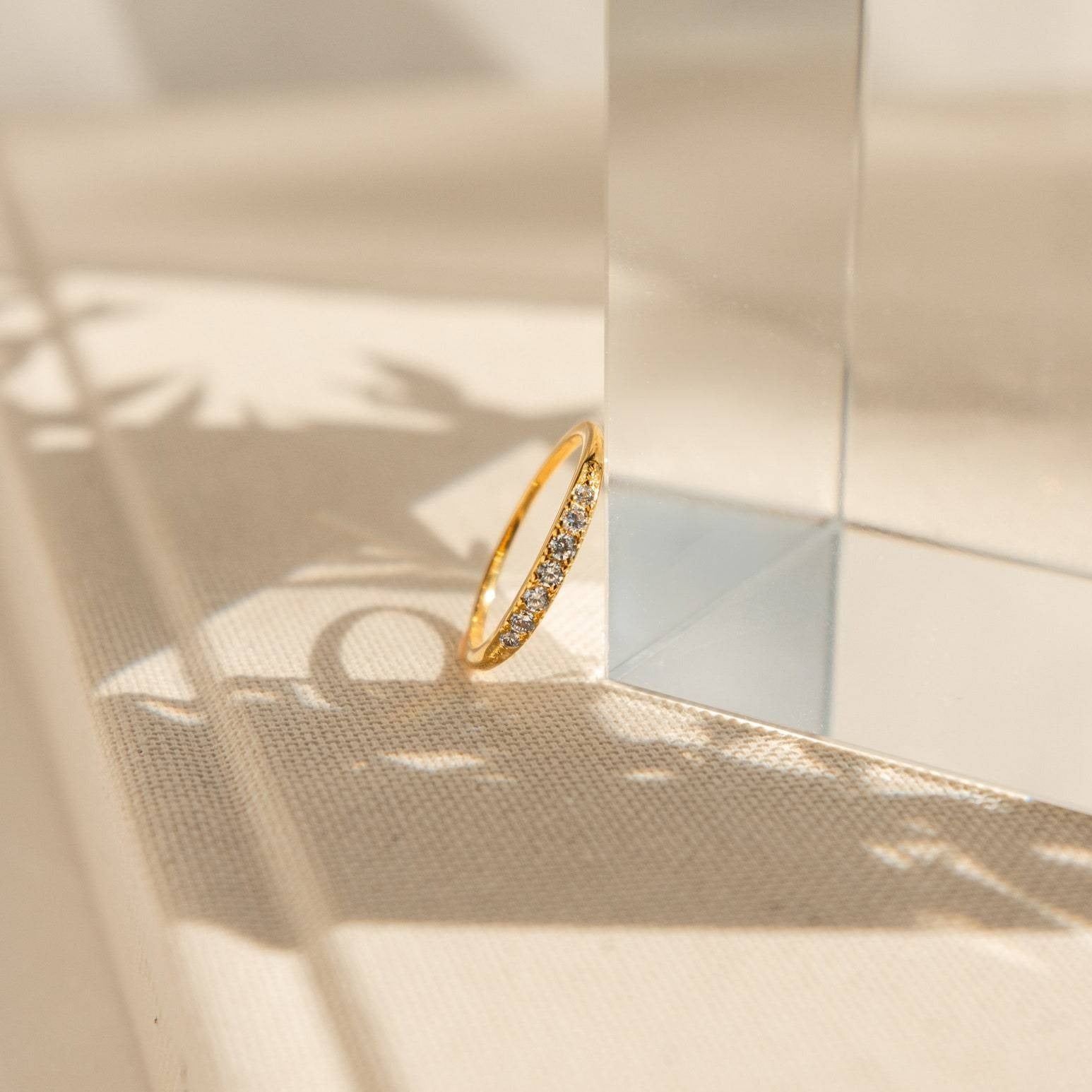 The Lace Pave Ring, a slim diamond band, is displayed on a clear glass block, its delicate shadow adding to its elegance.