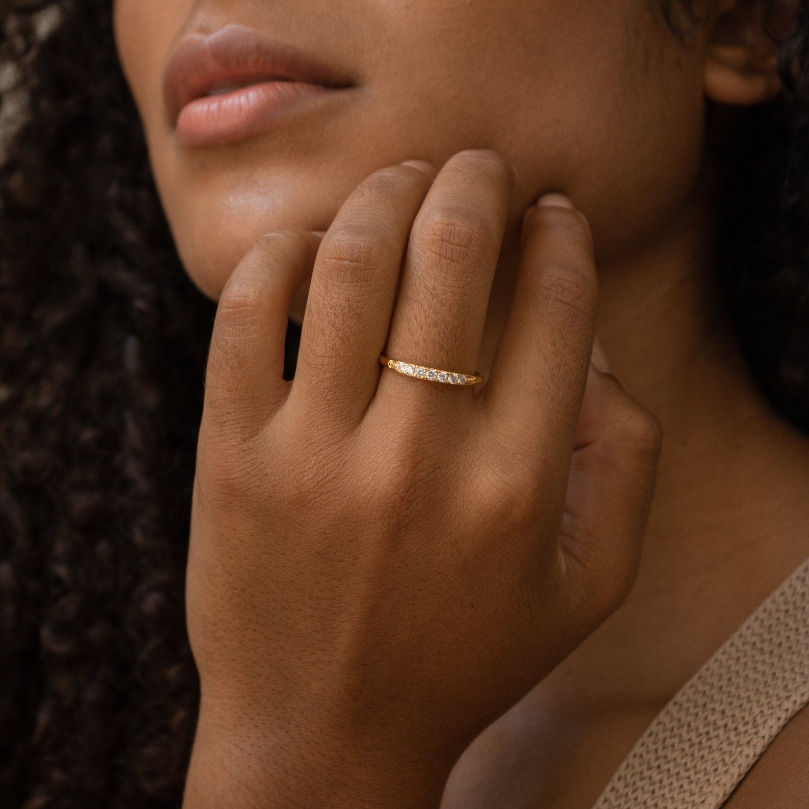 A woman with curly hair gently touches her face, wearing the delicate Lace Pave Ring on her finger.