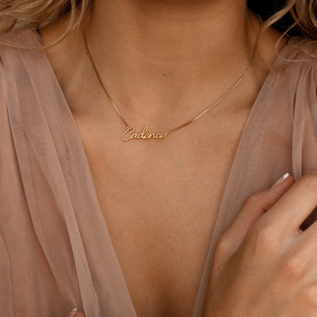 Nella Name Necklace in Box Chain with "Cadence," worn by a person in a sheer, light pink blouse.