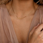 Nella Name Necklace in Box Chain with "Cadence," worn by a person in a sheer, light pink blouse.