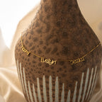 The Preppy Multiple Name Necklace in Box Chain, featuring Naomi, Evelyn, and Jessica in a youth-inspired font, is draped over a textured brown vase.