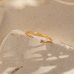 The Cecilia Pave Ring is a delicate open-style gold ring, featuring a small diamond atop a textured, light-colored stone surface.