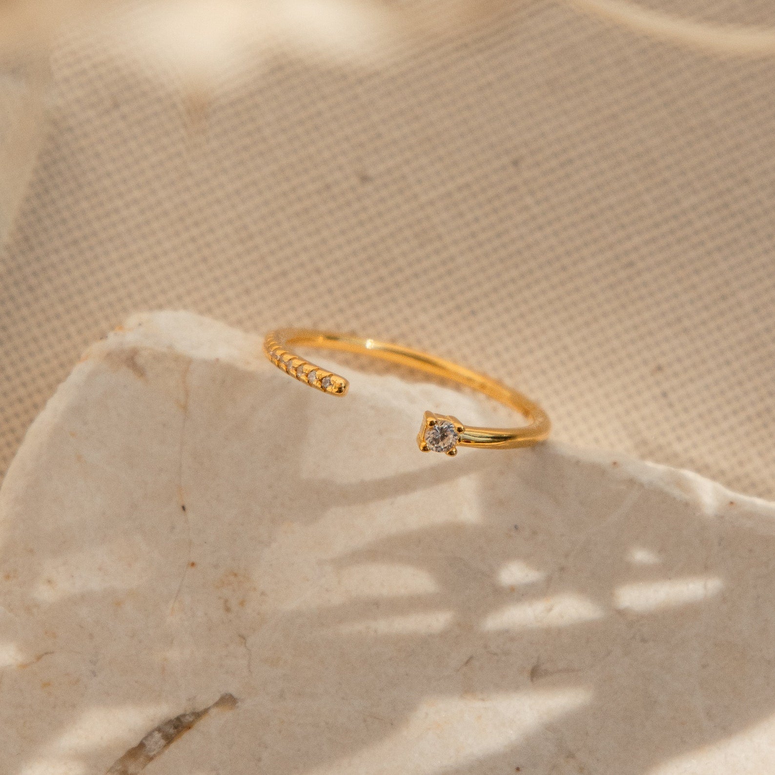 The Cecilia Pave Ring is a delicate open-style gold ring, featuring a small diamond atop a textured, light-colored stone surface.