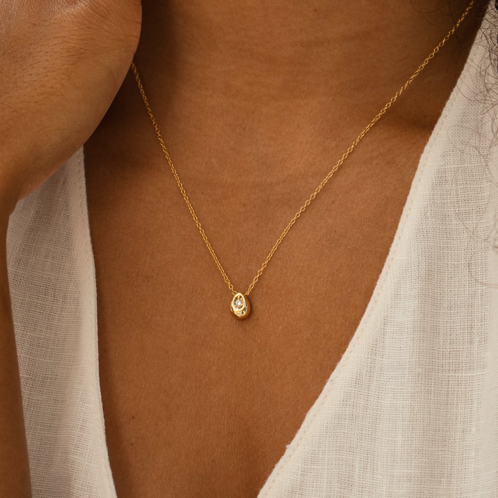 The Nugget Necklace, with its delicate pendant, sits elegantly on a white textured top and brings effortless sophistication to any outfit.