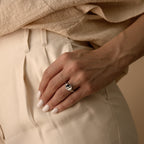 A hand with pale nail polish rests on cream pants, adorned with the Yin Yang Ring, crafted in silver and featuring an elegant enamel finish.