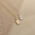 Two Pearl Locket Necklaces—one gold, one silver—each with a rectangular shape and mother of pearl inlay, are displayed on a neutral background.