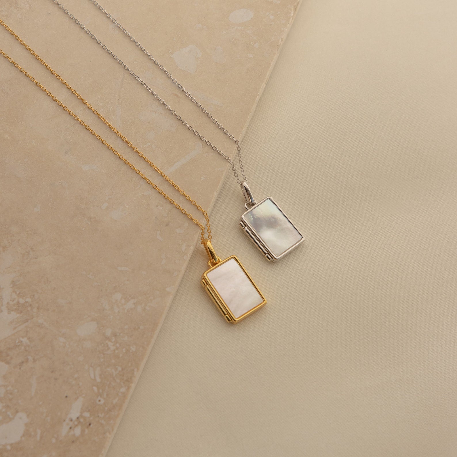 Two Pearl Locket Necklaces—one gold, one silver—each with a rectangular shape and mother of pearl inlay, are displayed on a neutral background.