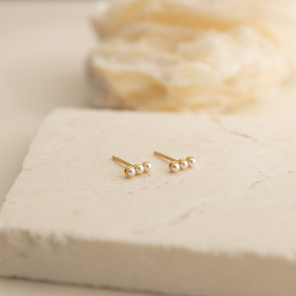Tiny Pearl Bar Studs feature three freshwater pearls each, ideal for everyday wear. Shown on a light stone surface with a softly blurred background.