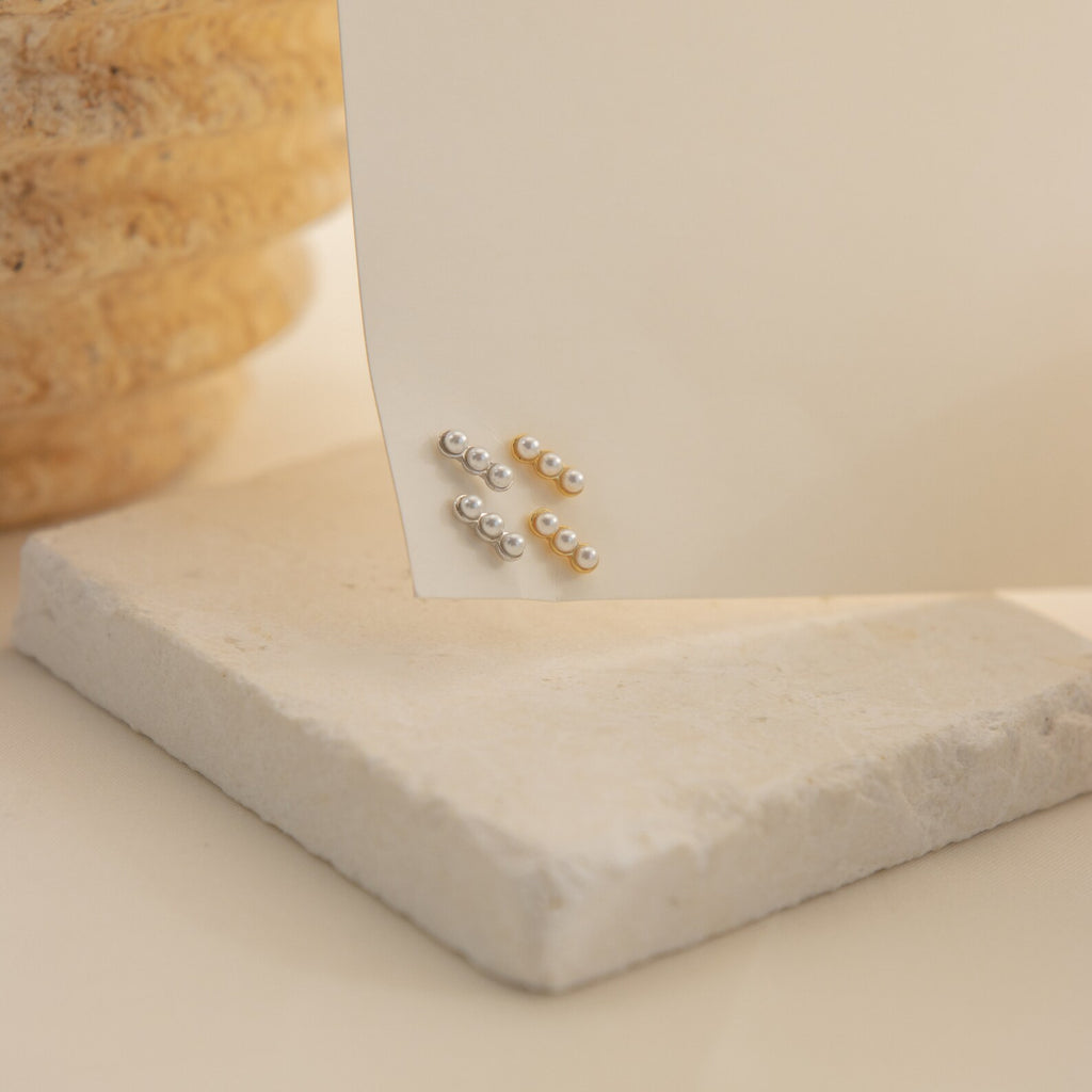 Tiny Pearl Bar Studs, ideal for daily wear, are displayed on a cream-colored card and set on a stone surface.