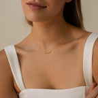 A woman in a white top wears the Tiny Preppy Name Necklace, a delicate gold piece featuring a customizable name plate pendant finished with a youthful, preppy font.
