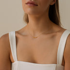 A woman in a white top wears the Tiny Preppy Name Necklace, a gold necklace with a small customizable nameplate charm in a youthful font.