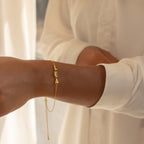 The Custom Letter Bracelet with "LEA" letters is shown on a wrist, paired with a cream long sleeve shirt—ideal for fans of personalized name jewelry.