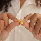 Close-up of hands holding a gold necklace with cursive name pendants, person wearing a white shirt and the Grace Duo Name Ring for a stylish, personalized touch.