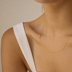 A woman wearing a Pave Sideways Initial Necklace with an S pendant and a white sleeveless top.